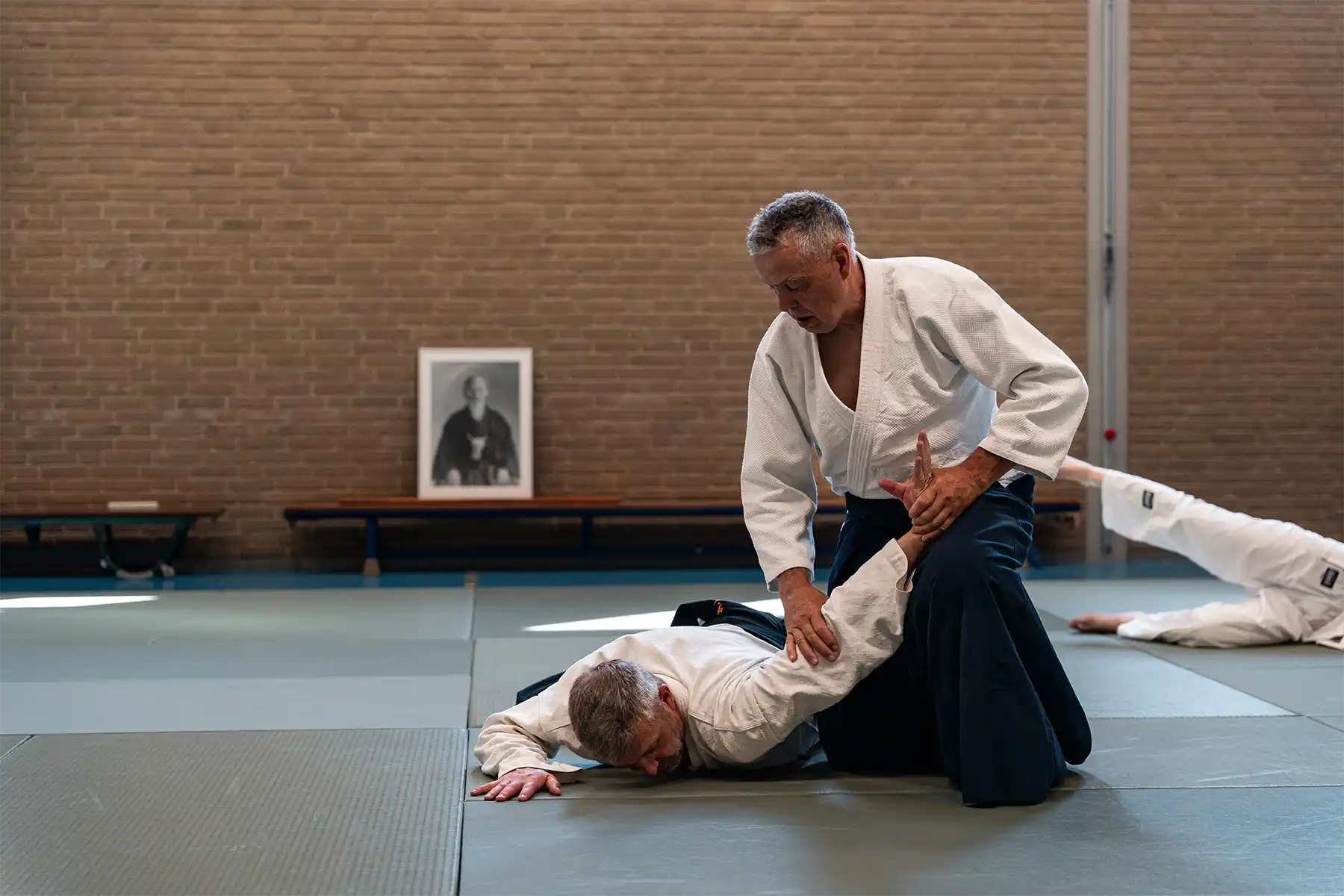 Aikido leraar demonstreert een controletechniek op de mat tijdens een rustige en respectvolle aikido training, gericht op techniek en samenwerking in plaats van vechten.